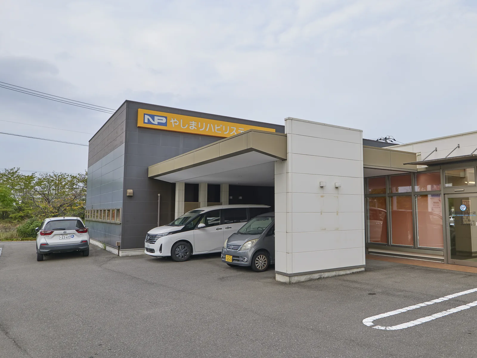 やしまリハビリステーションの外観。黄色い看板が掲げられた建物と、車寄せのある入口